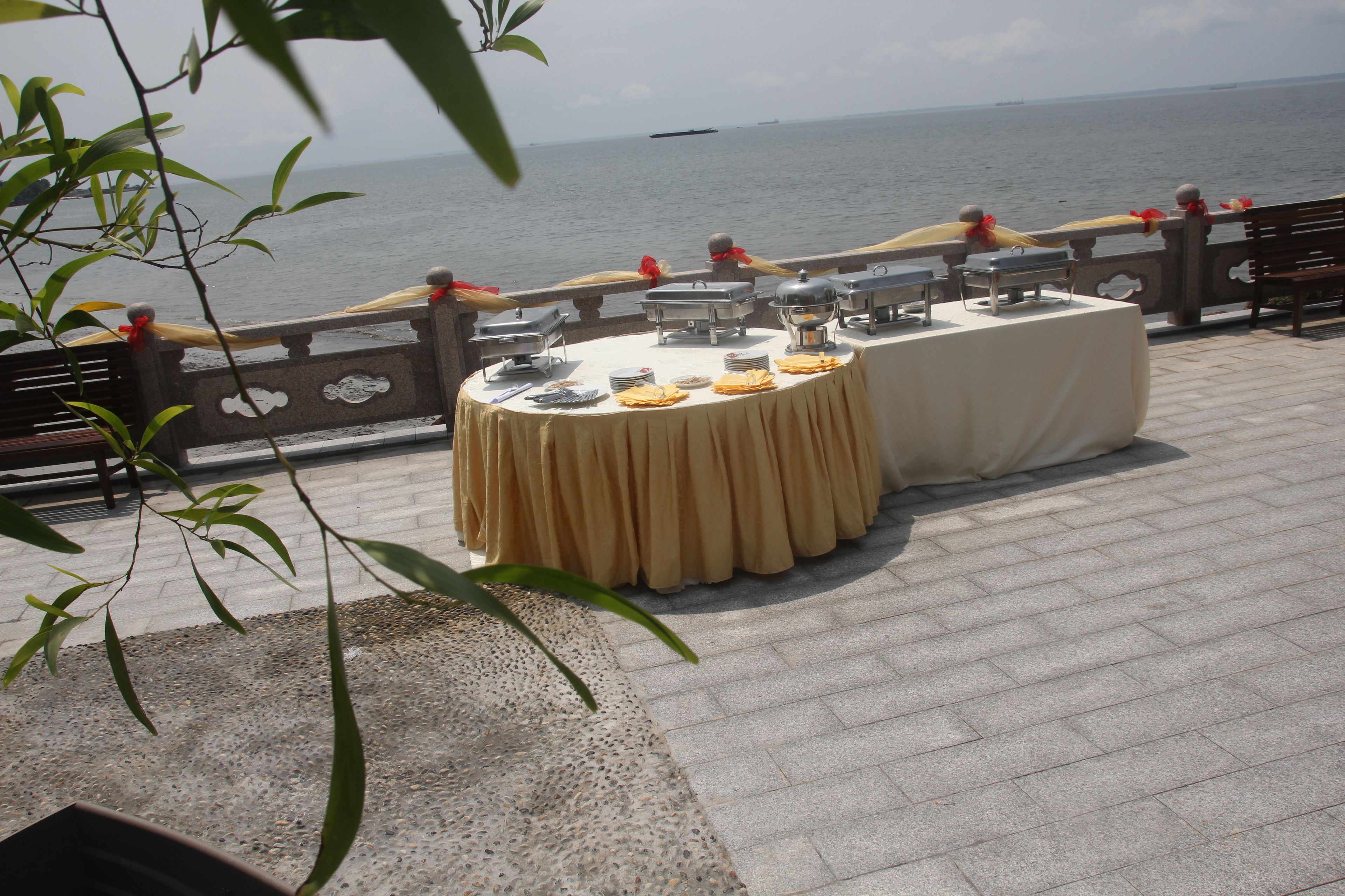 A table set up with a tablecloth and food service items, overlooking a body of water.
