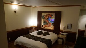 Una habitación de hotel con cama, mesita de noche, lámpara, sillón y un cuadro en la pared.