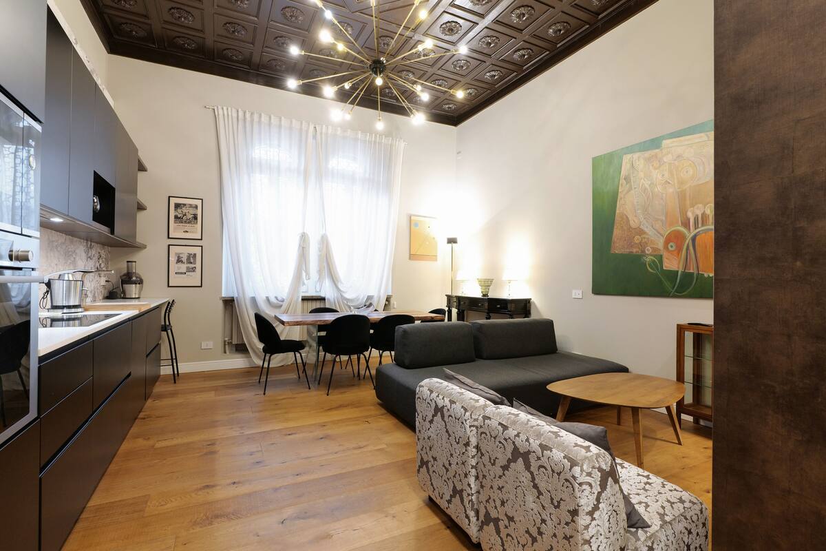 A modern living room with a sofa, a dining table, and a kitchen area.