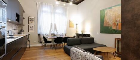 A modern living room with a sofa, a dining table, and a kitchen area.