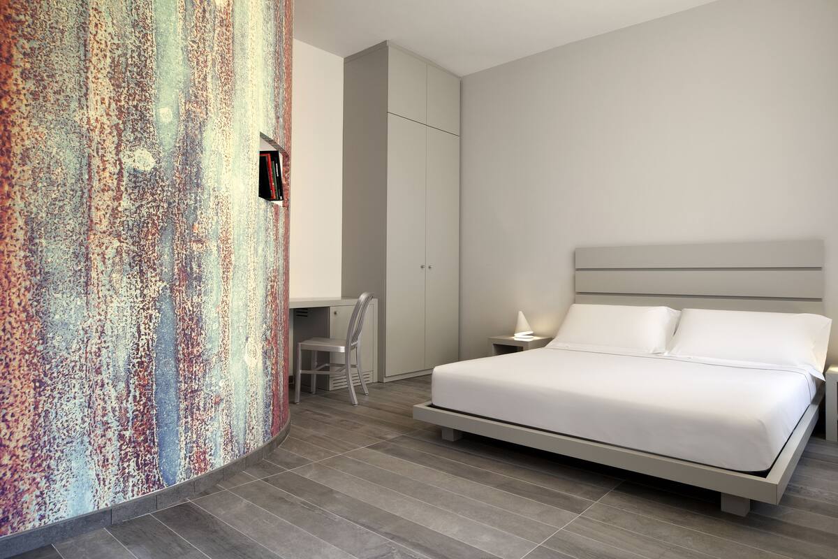 A modern bedroom with a bed, bedside tables, a desk, and a wardrobe.
