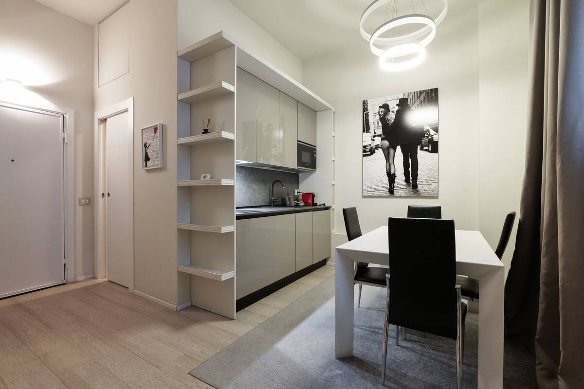 A compact kitchen with integrated storage, a dining area with a table and chairs, and a modern pendant light fixture.