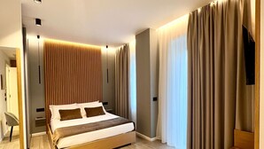 A modern bedroom with a wooden bed, a TV, and a seating area. - La Chambre Milano (Milan)