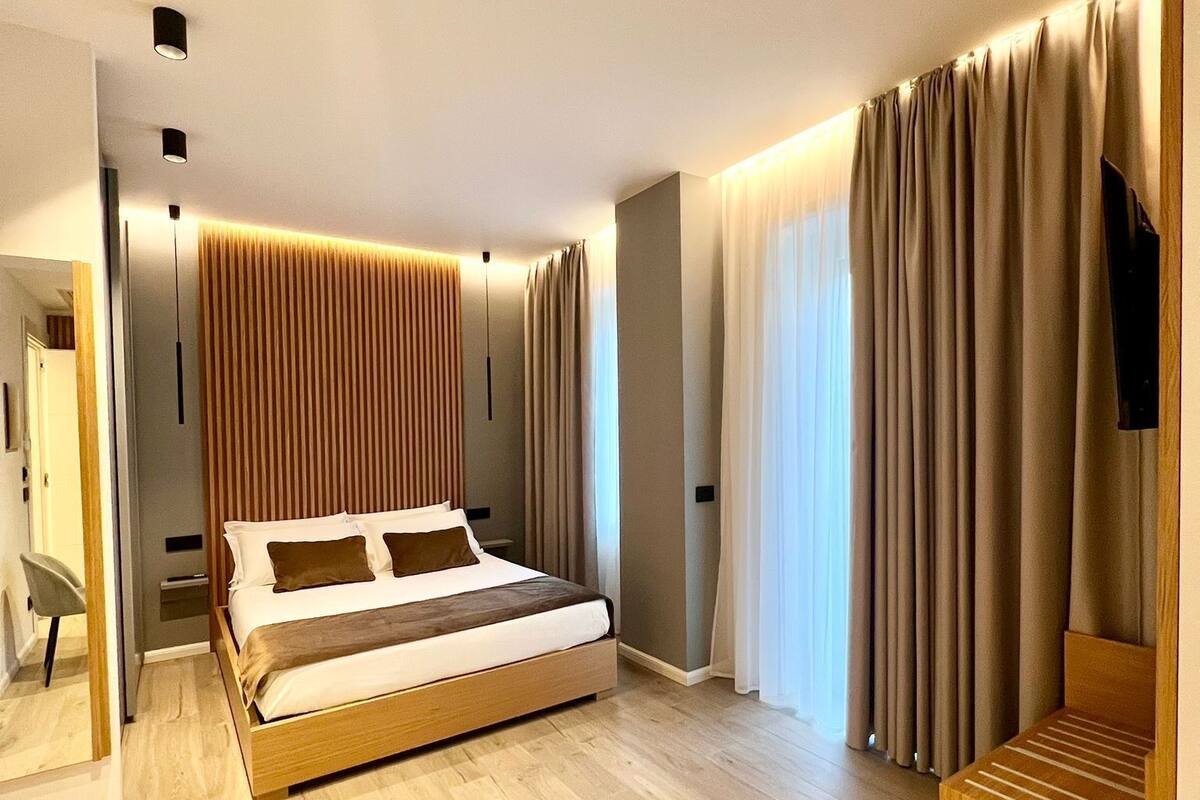 A modern bedroom with a wooden bed, a TV, and a seating area.