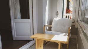 A narrow hallway with a wooden bench and a white chair, leading to a room with a white door and a window with a view of flowers. - Urban House Hostel (San Sebastián)