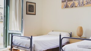 A room with two beds, a window with curtains, a painting on the wall, and a colorful rug on the floor. - Urban House Hostel (San Sebastián)