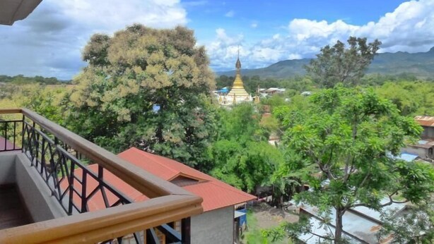 A view from a balcony overlooking a temple with a golden spire, surrounded by lush greenery and a mountainous backdrop. - Golden Lotus Inle Hotel (Nyaungshwe)