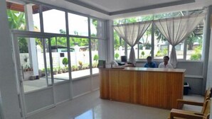 A reception area with a wooden desk, two chairs, and large windows with curtains. - Golden Lotus Inle Hotel (Nyaungshwe)