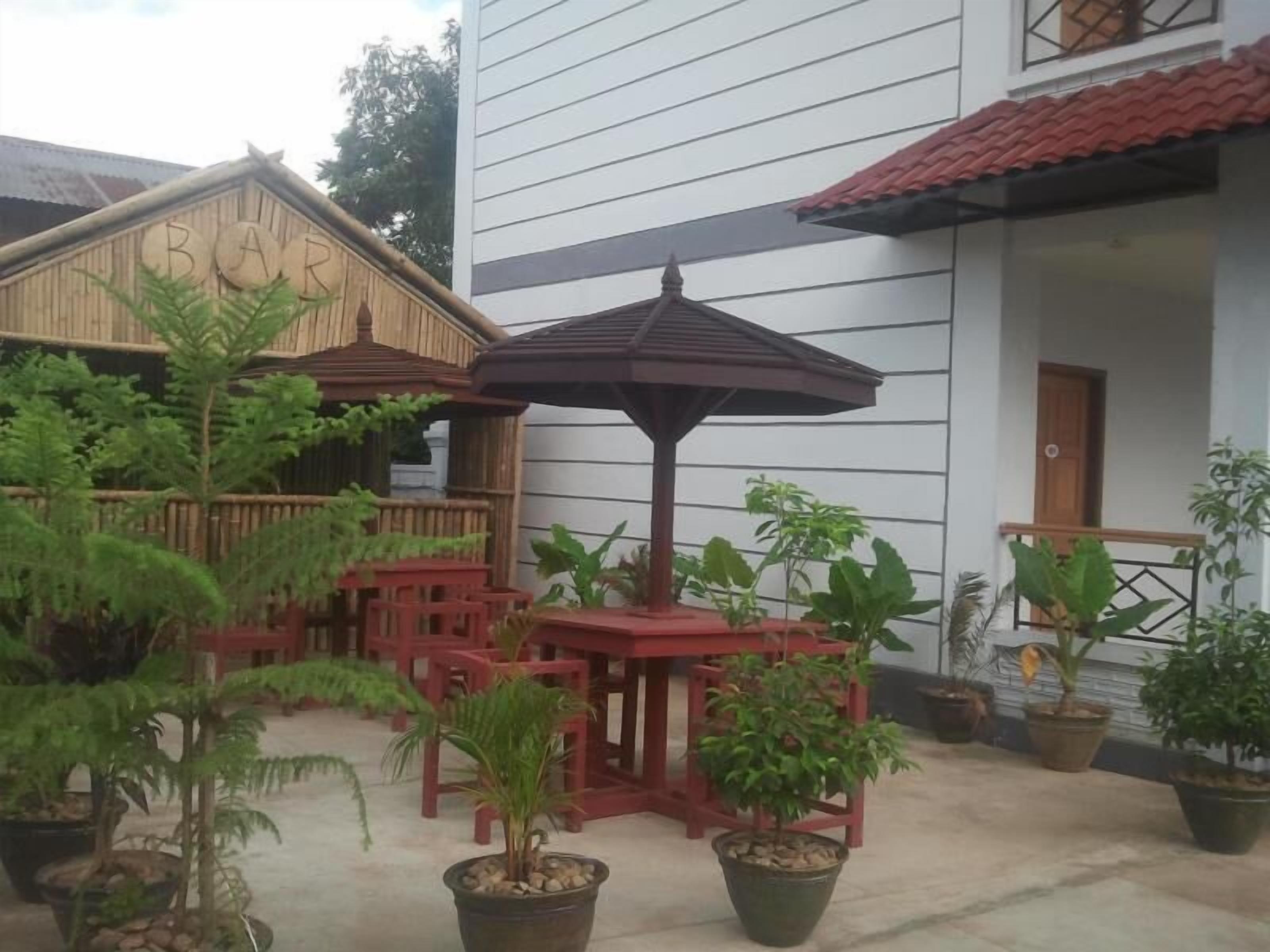 Un patio con plantas en macetas, mobiliario exterior y una estructura de madera con la leyenda 'BAR'.