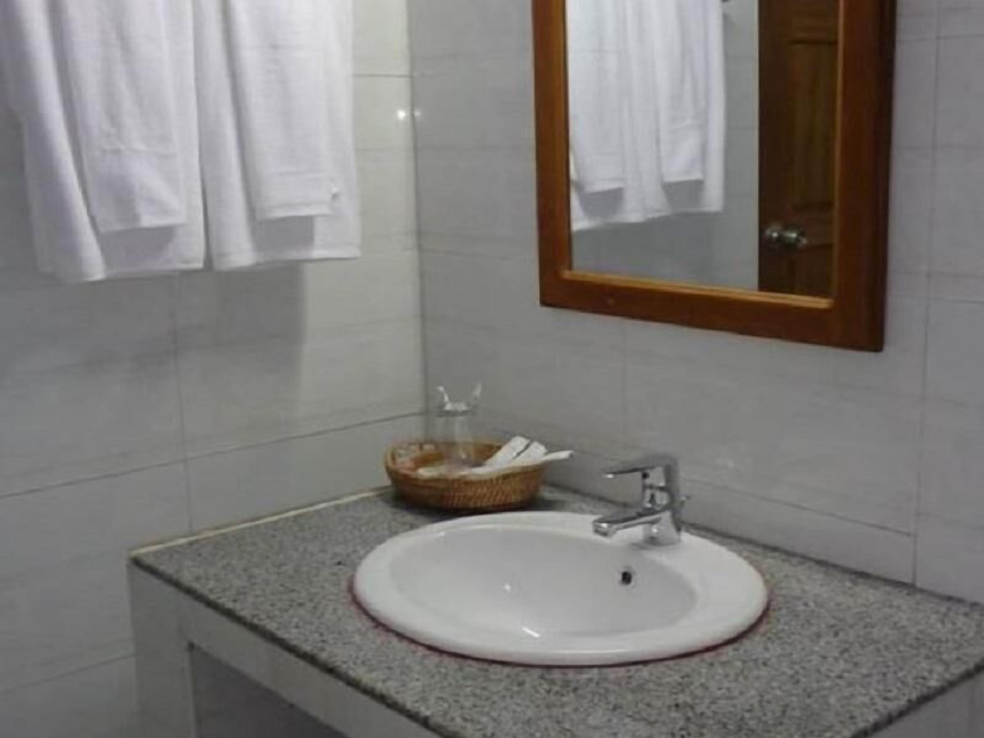 Un baño con un lavamanos blanco, un espejo con marco de madera y una cesta de artículos de aseo.