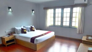 A hotel room with a wooden bed, a nightstand, a desk, and a window with curtains. - Golden Lotus Inle Hotel (Nyaungshwe)