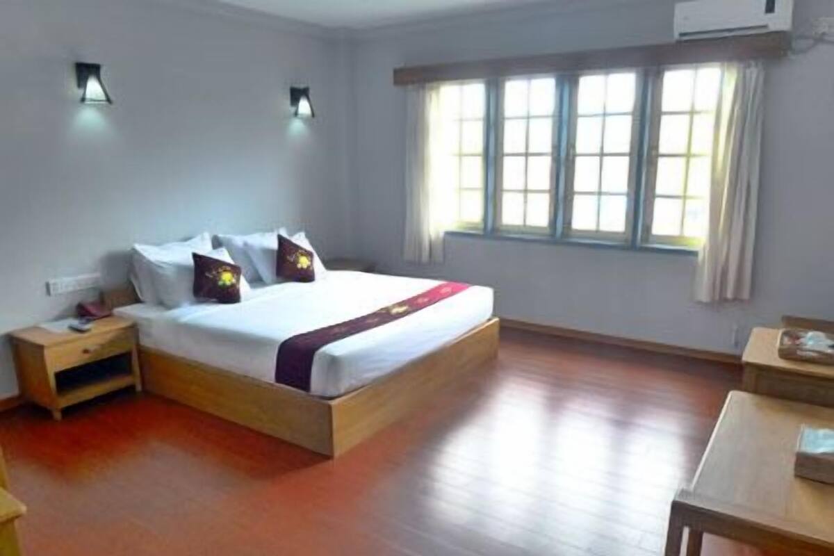 A hotel room with a wooden bed, a nightstand, a desk, and a window with curtains.