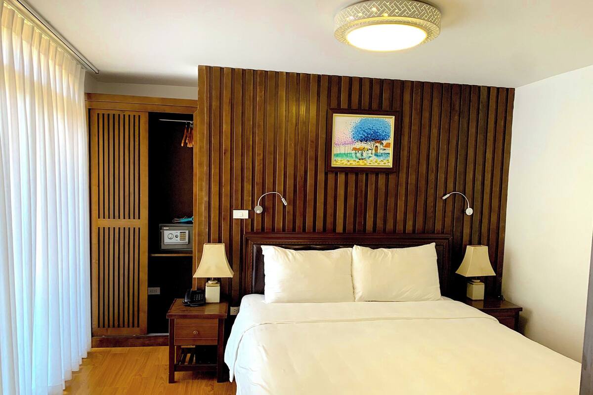 Een hotelkamer met een wand van houten panelen, een bed met witte lakens, twee bedlampen en een schilderij boven het bed.