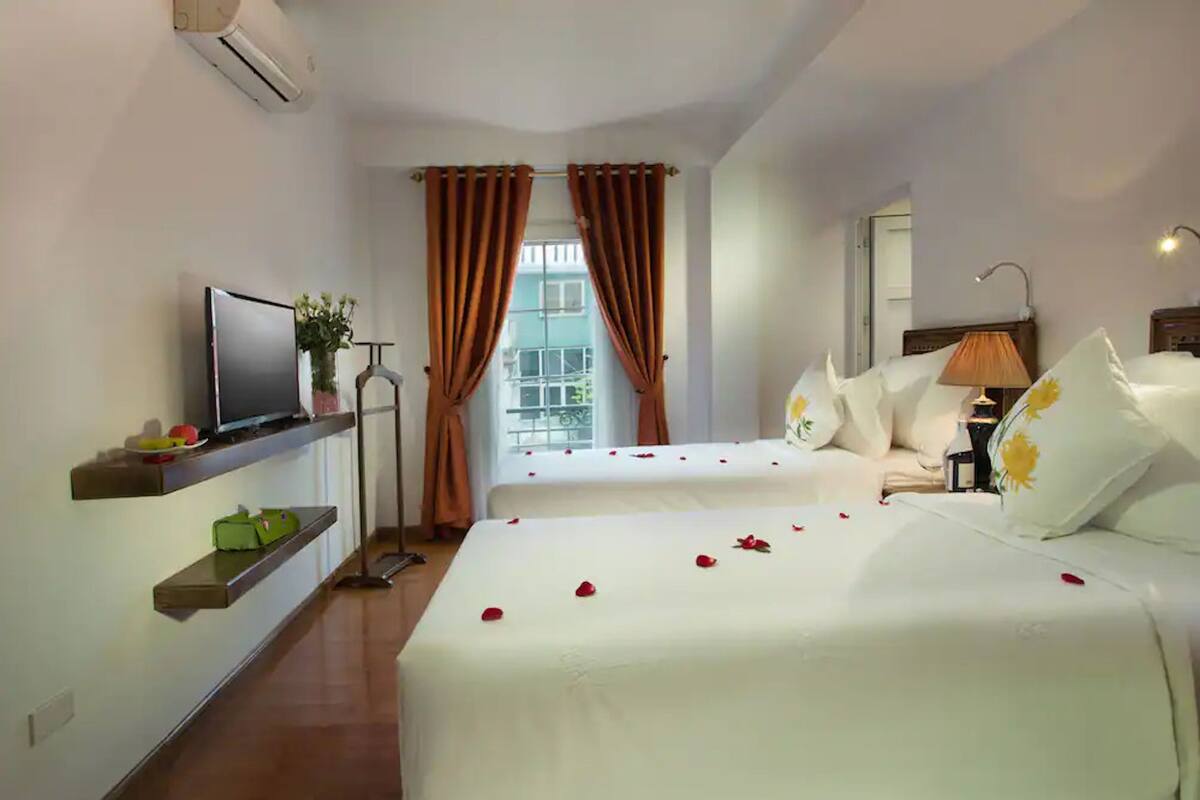 Een hotelkamer met twee bedden, een tv op een plank, een raam met gordijnen en een lamp.