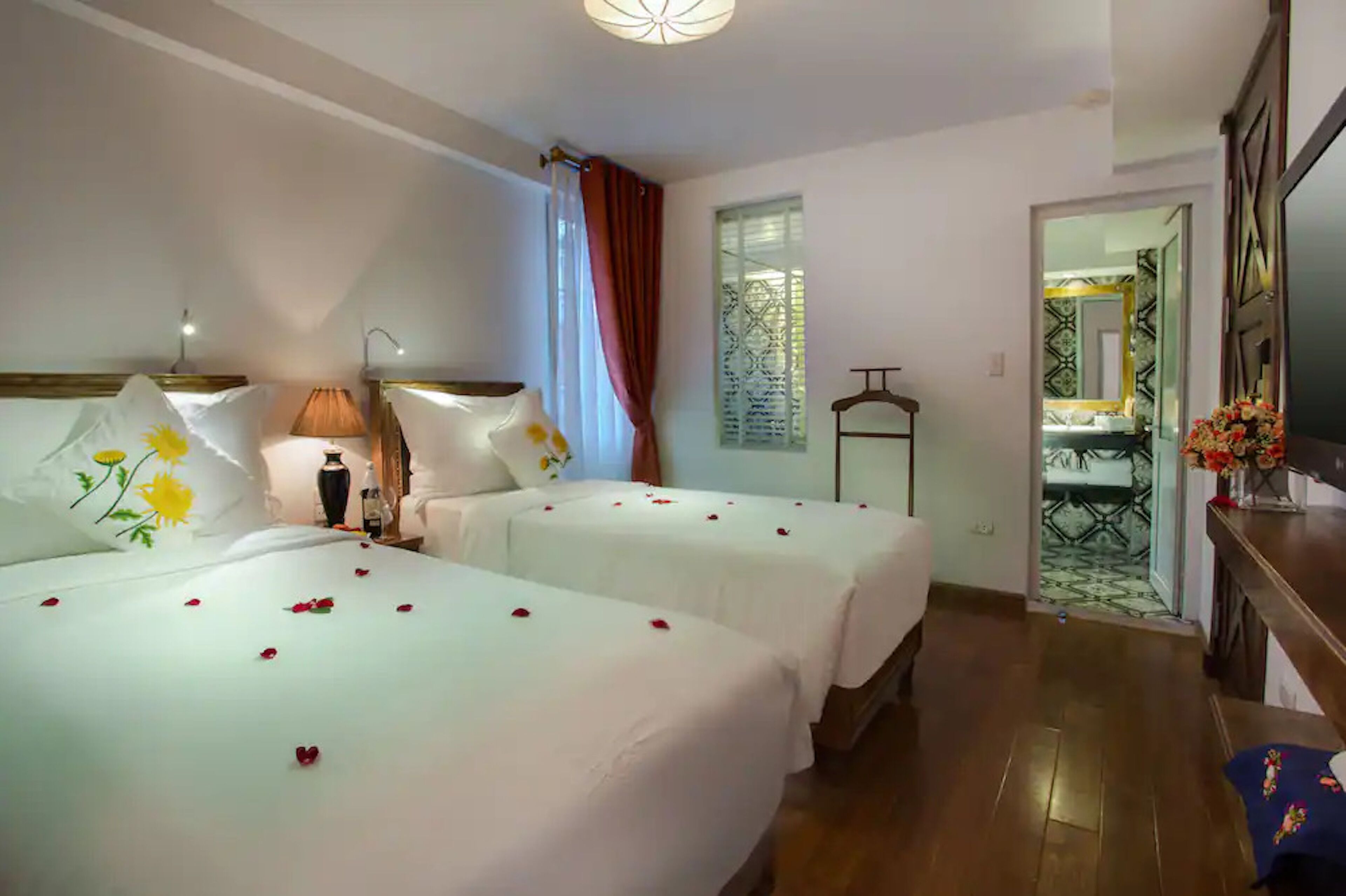 A hotel room with two beds, a bedside table, a lamp, and a view of the bathroom through a door.