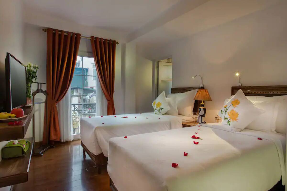Een hotelkamer met twee bedden, een zithoek, een televisie en een balkon met gordijnen.
