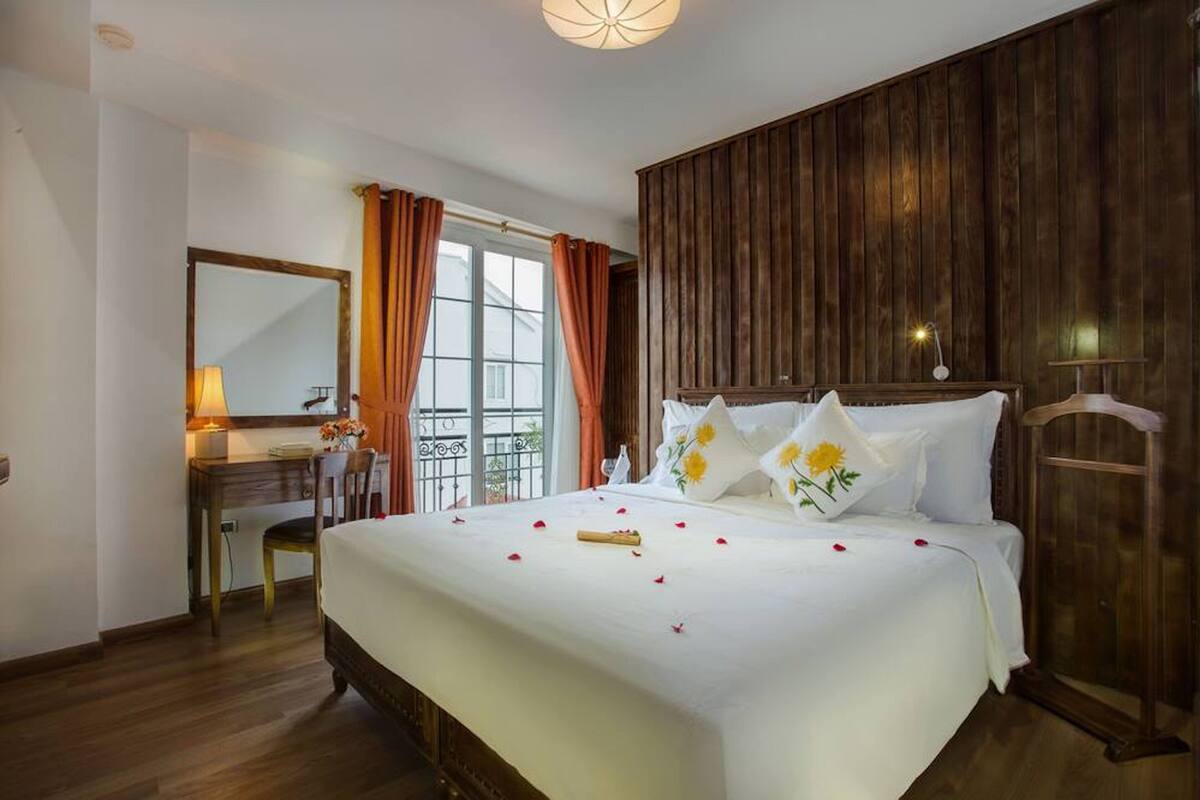 Een hotelkamer met een groot bed, een bureau met stoel, een spiegel en een wand van houten panelen.