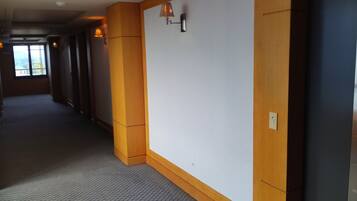A hotel corridor with wooden paneling, a large white wall, and a window at the end.