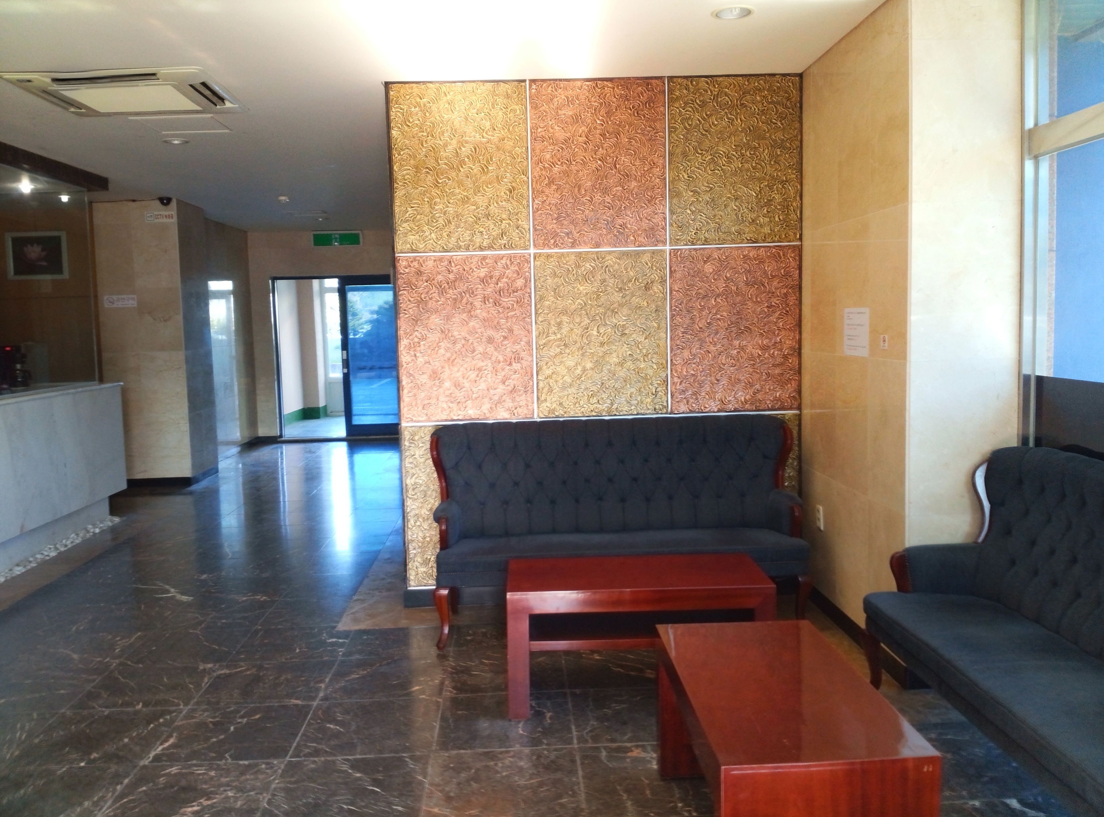 A lobby with a reception desk, a dark upholstered sofa, a wooden coffee table, and a patterned wall.