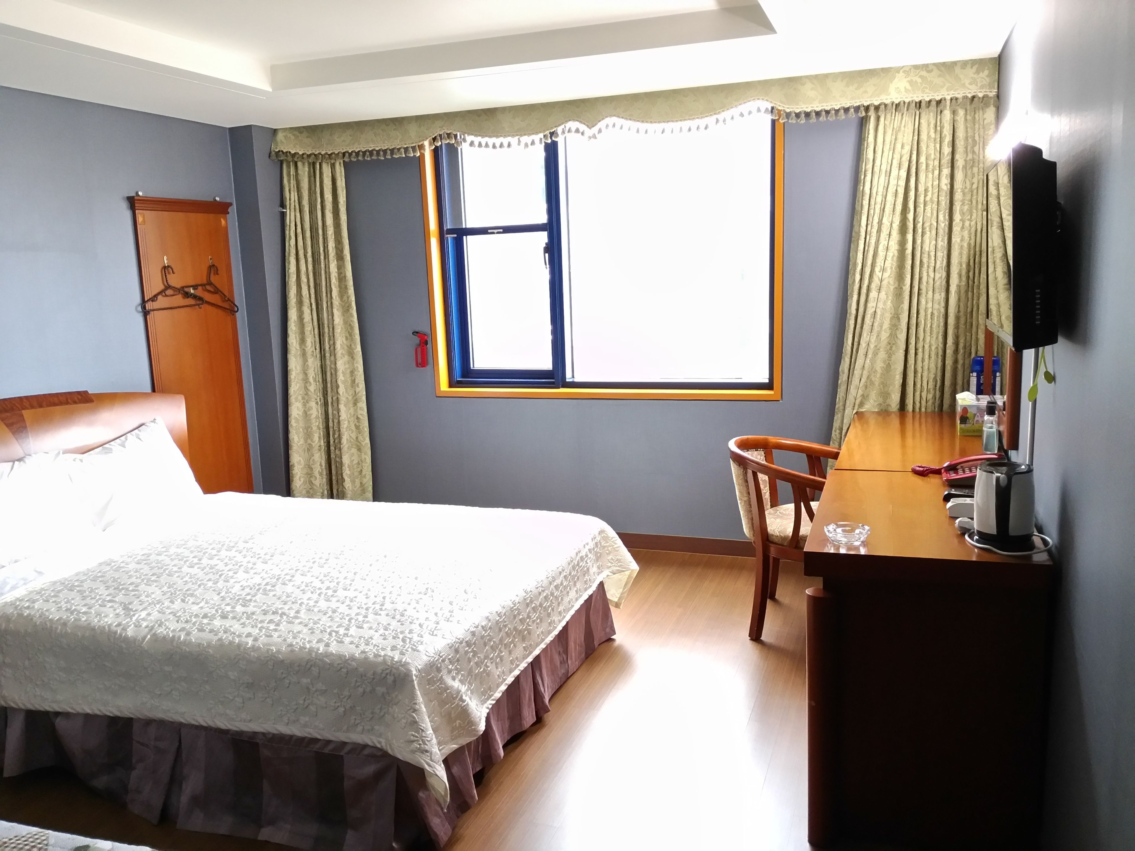 A hotel room with a bed, a desk with a chair, a television, and a window with curtains.