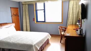 A hotel room with a bed, a desk with a chair, a television, and a window with curtains.