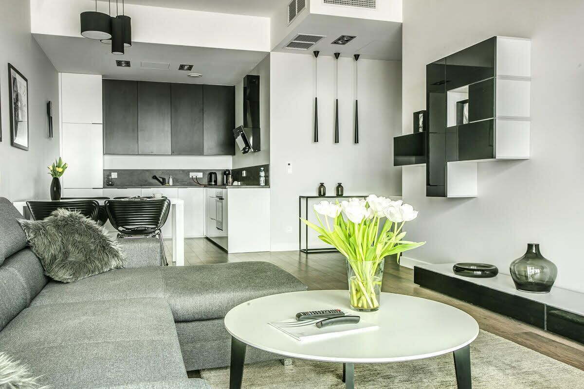 A modern living room with a grey sofa, a round coffee table, and a vase of white flowers.