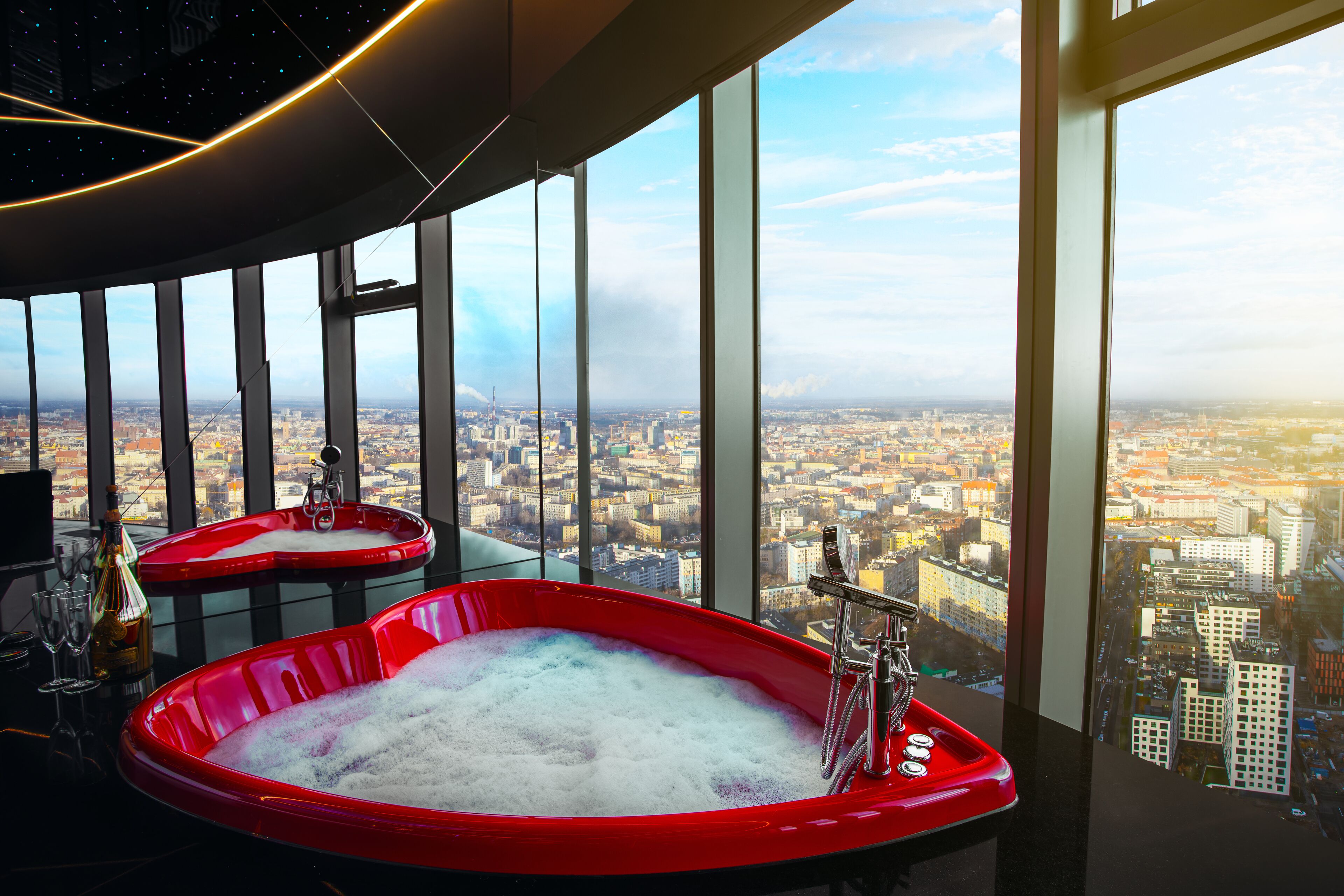 A high-rise hotel room with a city view, two red tubs, and a large window.