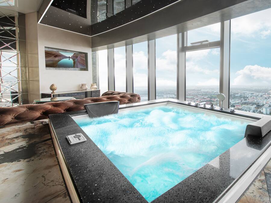Una piscina interior moderna con vistas a la ciudad, un ventanal grande y un sofá de cuero marrón.