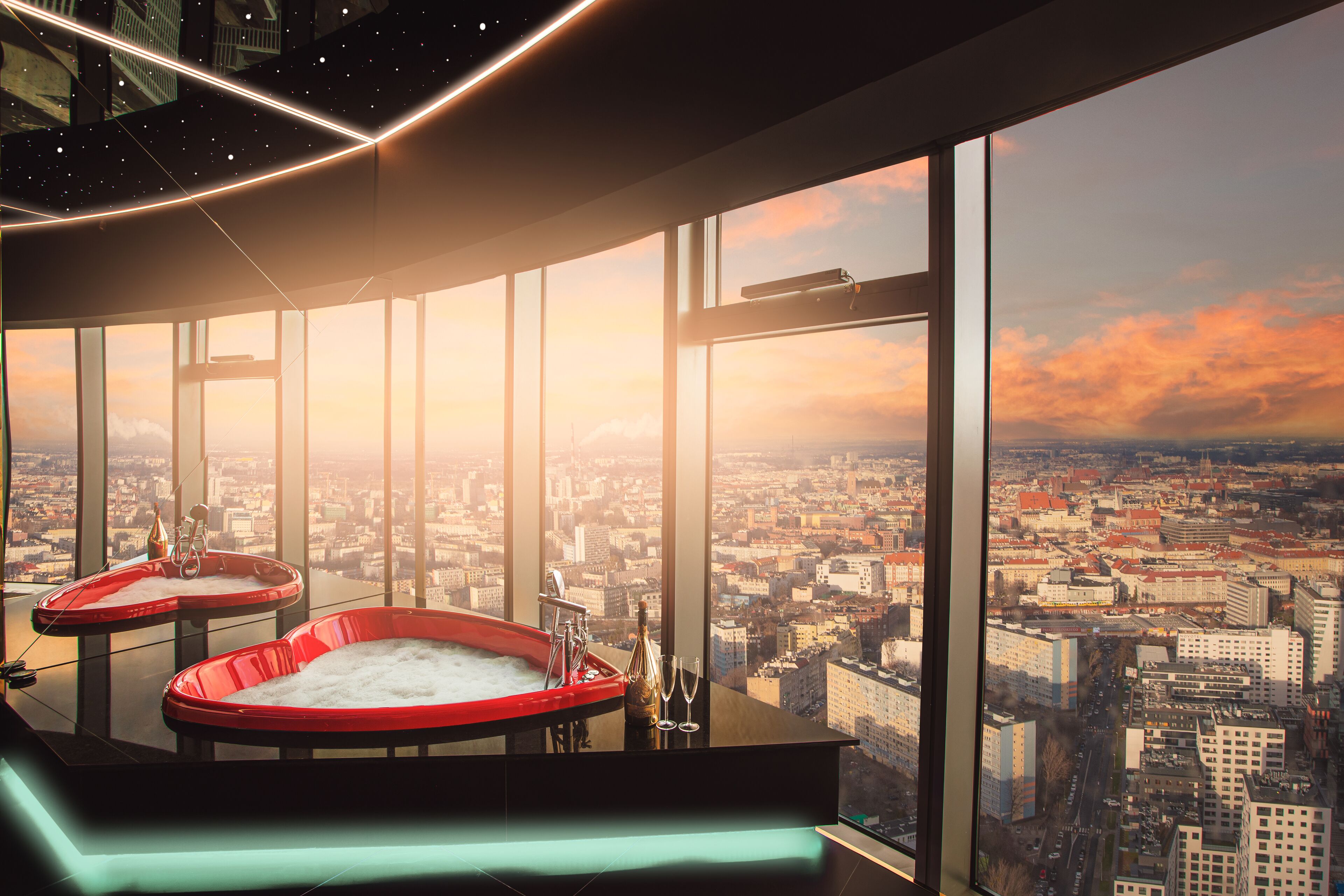 A high-rise hotel room with a city view, two red hot tubs, and a large window.