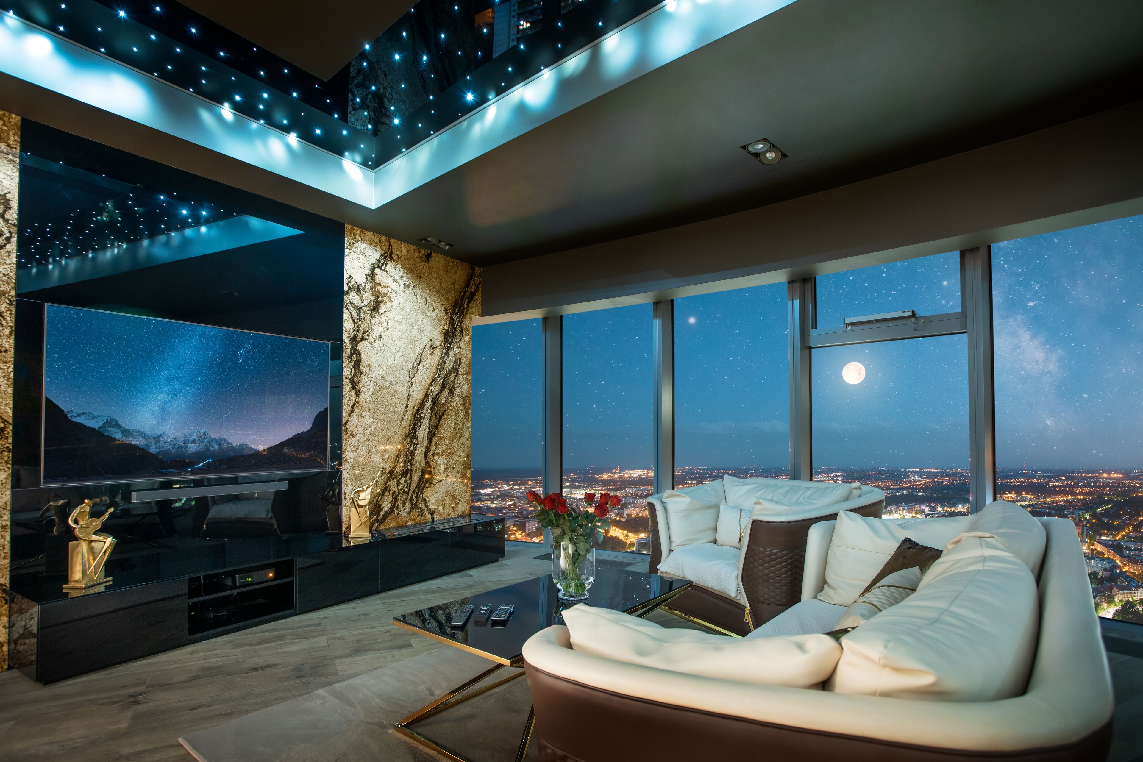 Un salon moderne doté d’un grand téléviseur, de sièges confortables et offrant une vue sur la ville grâce à de grandes fenêtres.