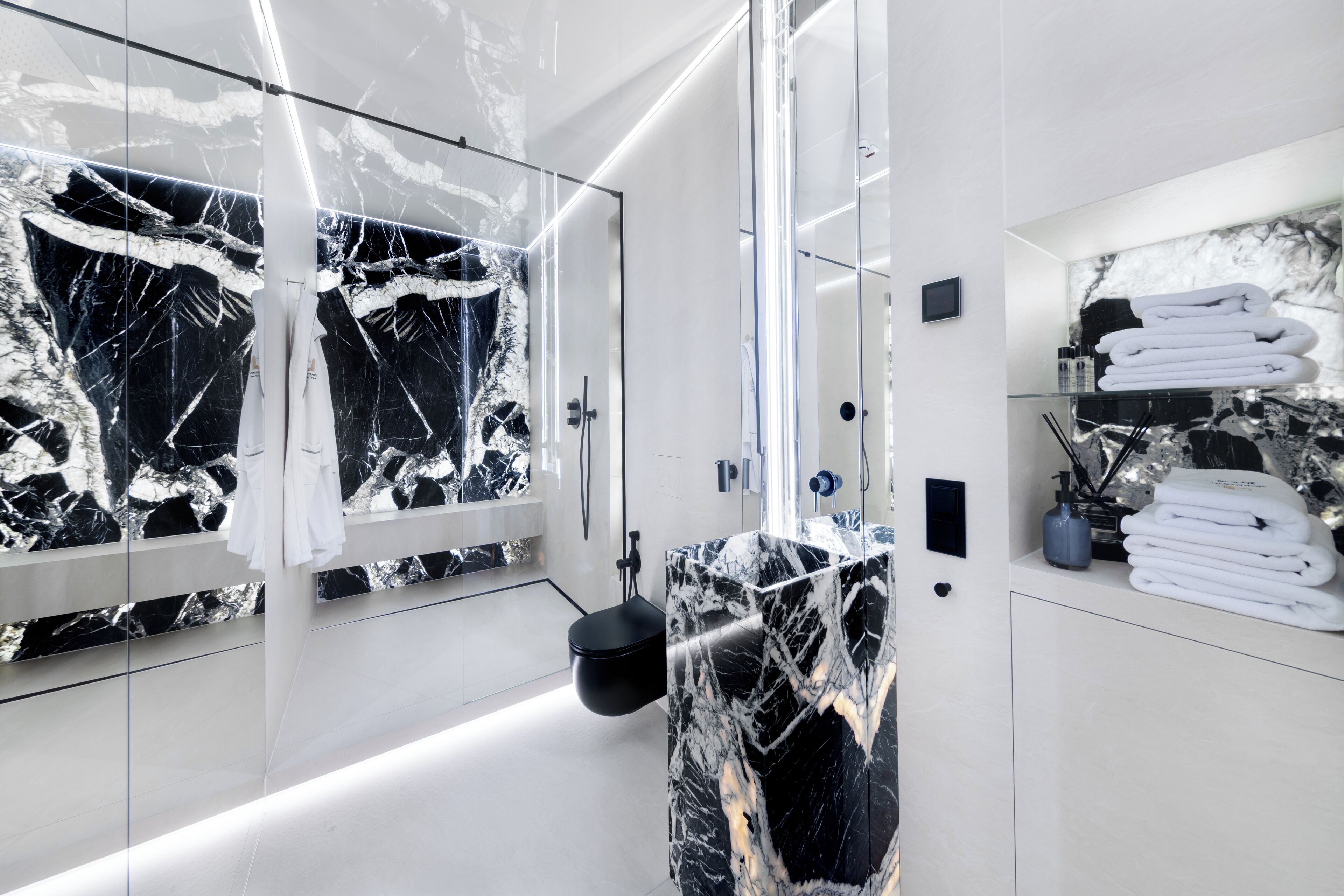 A modern bathroom with a glass shower enclosure, a marble vanity, and neatly folded towels on a shelf.