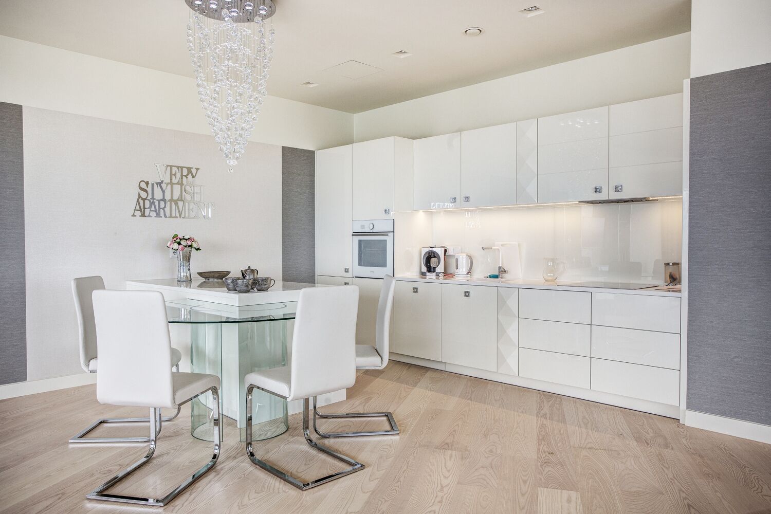 A modern kitchen with white cabinetry, a glass dining table, and a chandelier.