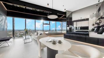 A modern living room with a large window, a sofa, a coffee table, and a dining area.