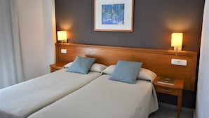 Un lit double avec deux oreillers, une table de chevet avec une lampe, un tableau encadré au mur et une prise de courant sur la table de chevet.