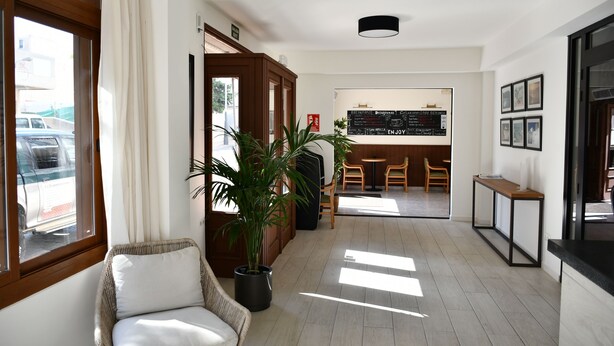 Un hall d’hôtel avec un fauteuil en osier, une plante en pot, un comptoir d’accueil et un menu affiché au mur.