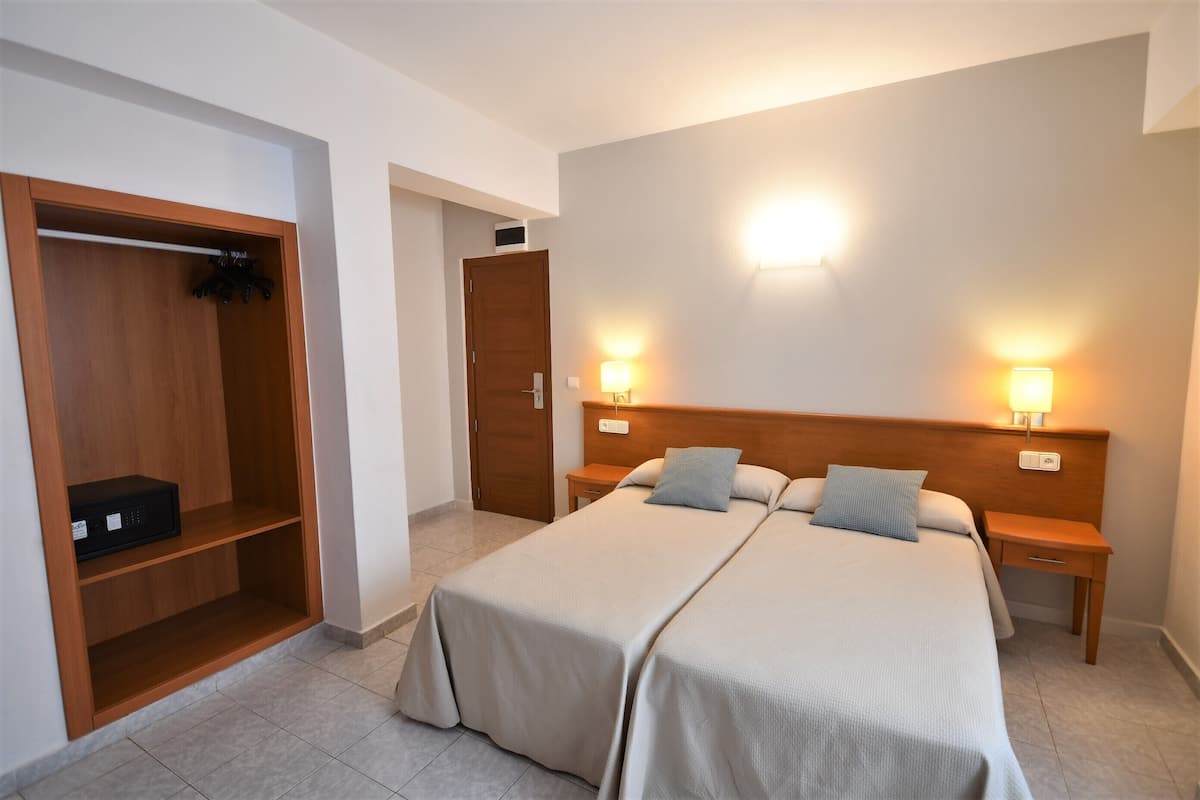 Ein Hotelzimmer mit zwei Betten, einem Kleiderschrank, einem Nachttisch mit Lampe und einer Wandleuchte.