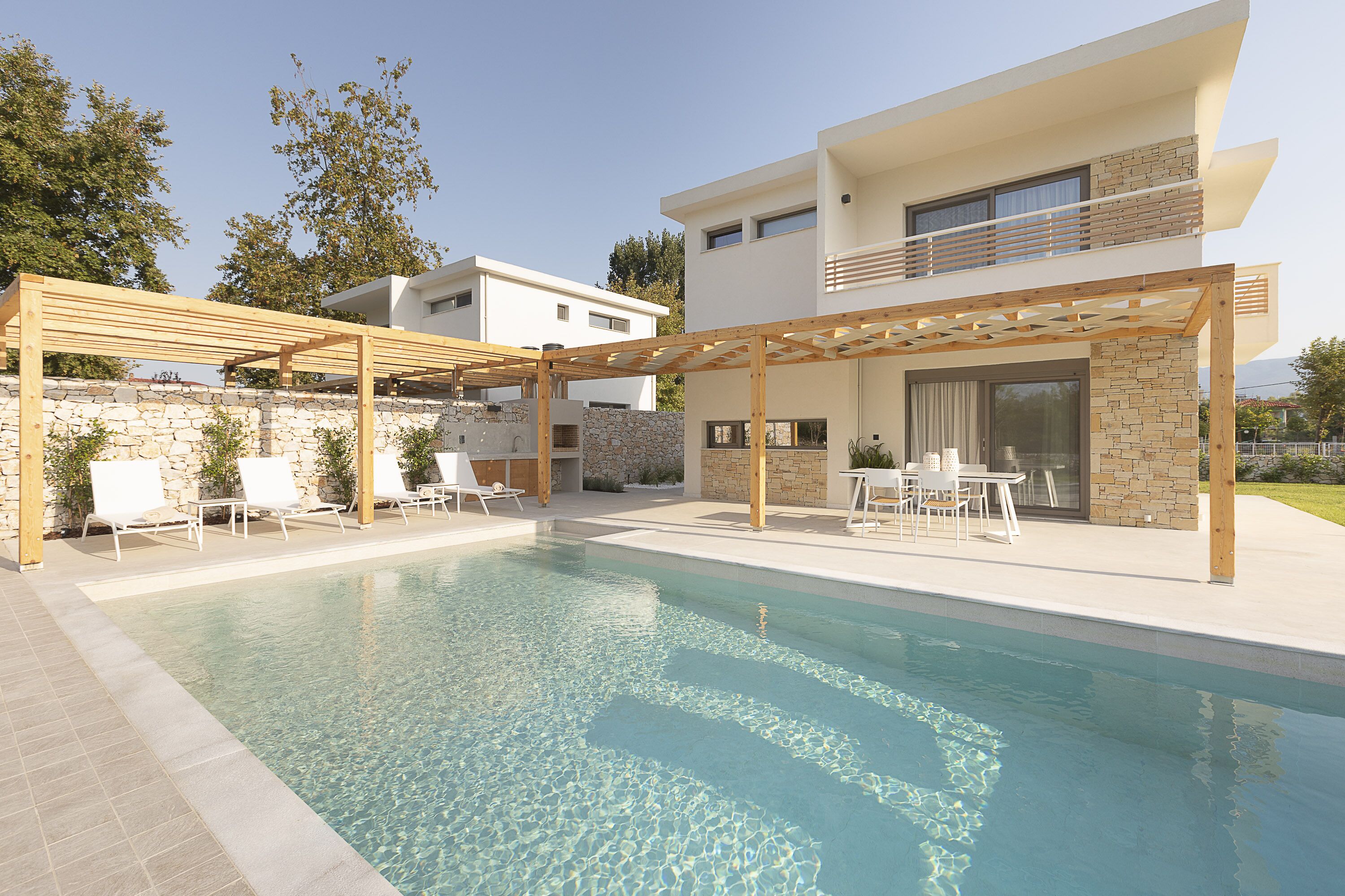 A modern pool area with a pergola, lounge chairs, and a stone wall.