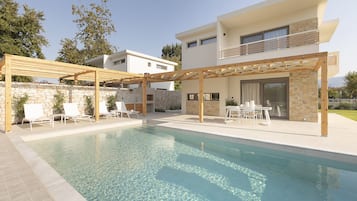 A modern pool area with a pergola, lounge chairs, and a stone wall.