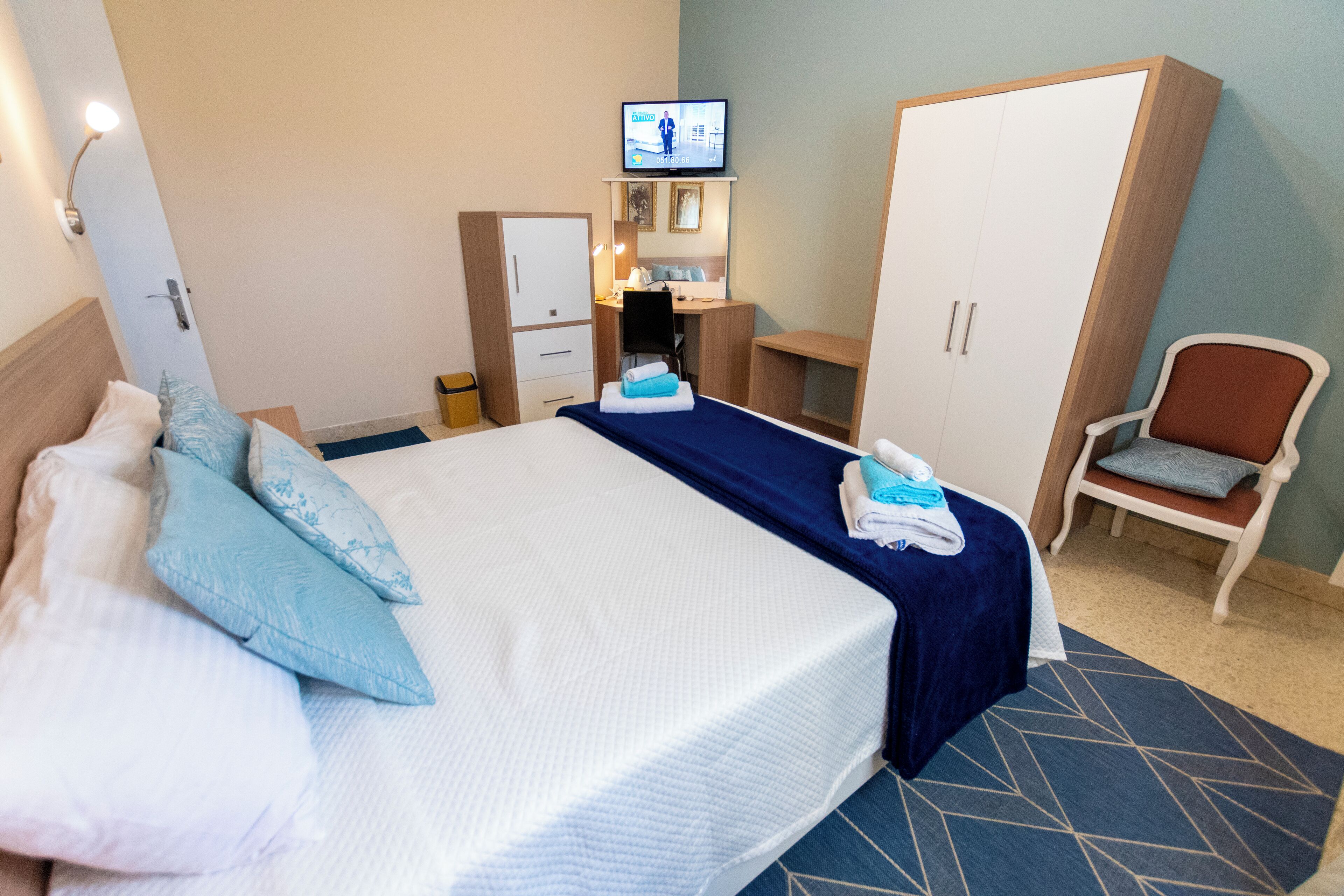 A hotel room with a bed, a desk, a wardrobe, a television, and a chair.