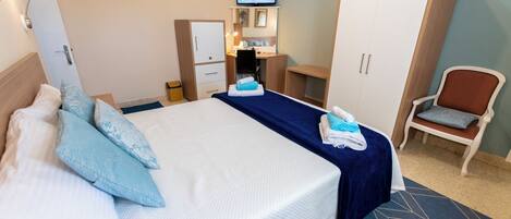 A hotel room with a bed, a desk, a wardrobe, a television, and a chair.
