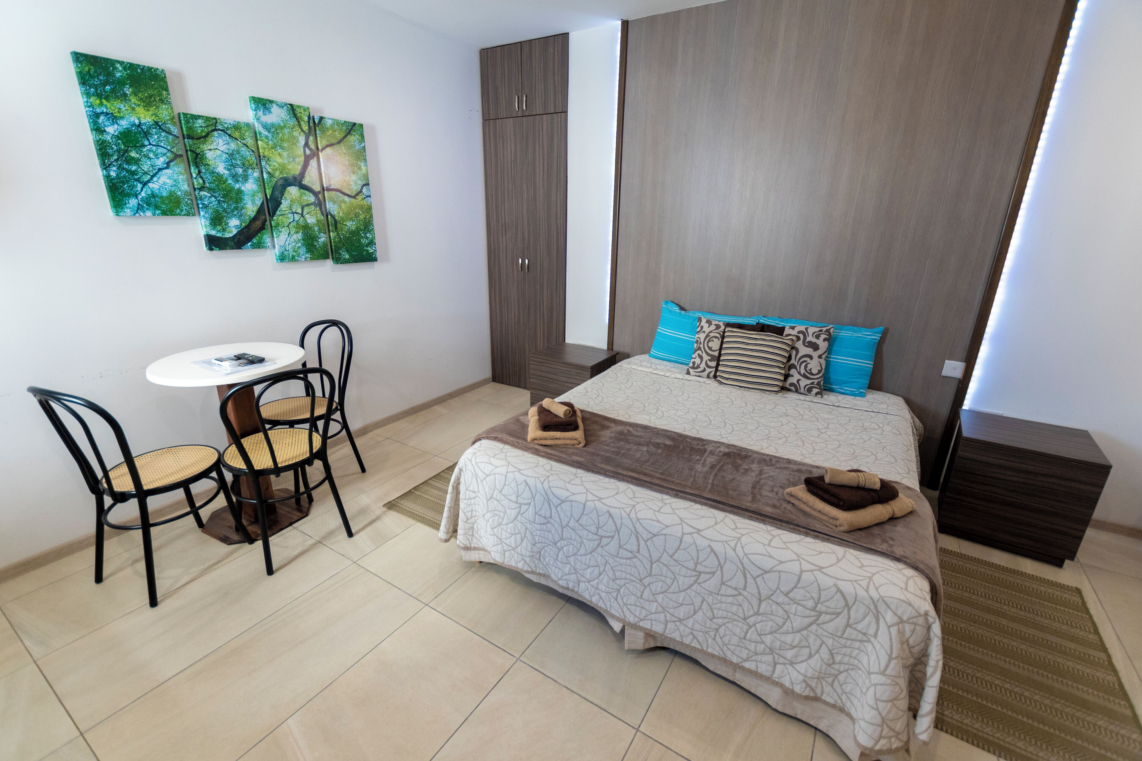 A bedroom with a bed, a small table with chairs, and two wall-mounted paintings.