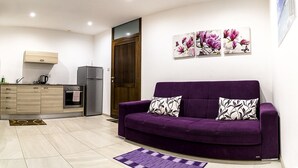 A modern kitchen with a purple sofa, wooden cabinets, and a refrigerator. - Estrella Lodging (Rabat)