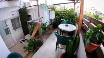 A small balcony with a table and chairs, surrounded by potted plants and a wooden structure.