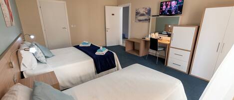 A hotel room with two beds, a desk, a chair, a television, and a wardrobe.