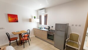 A compact kitchen with a dining table, chairs, a refrigerator, and a window with curtains. - Estrella Lodging (Rabat)
