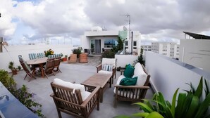 Eine Dachterrasse mit Holzmöbeln, Topfpflanzen und Blick auf die Stadtlandschaft.