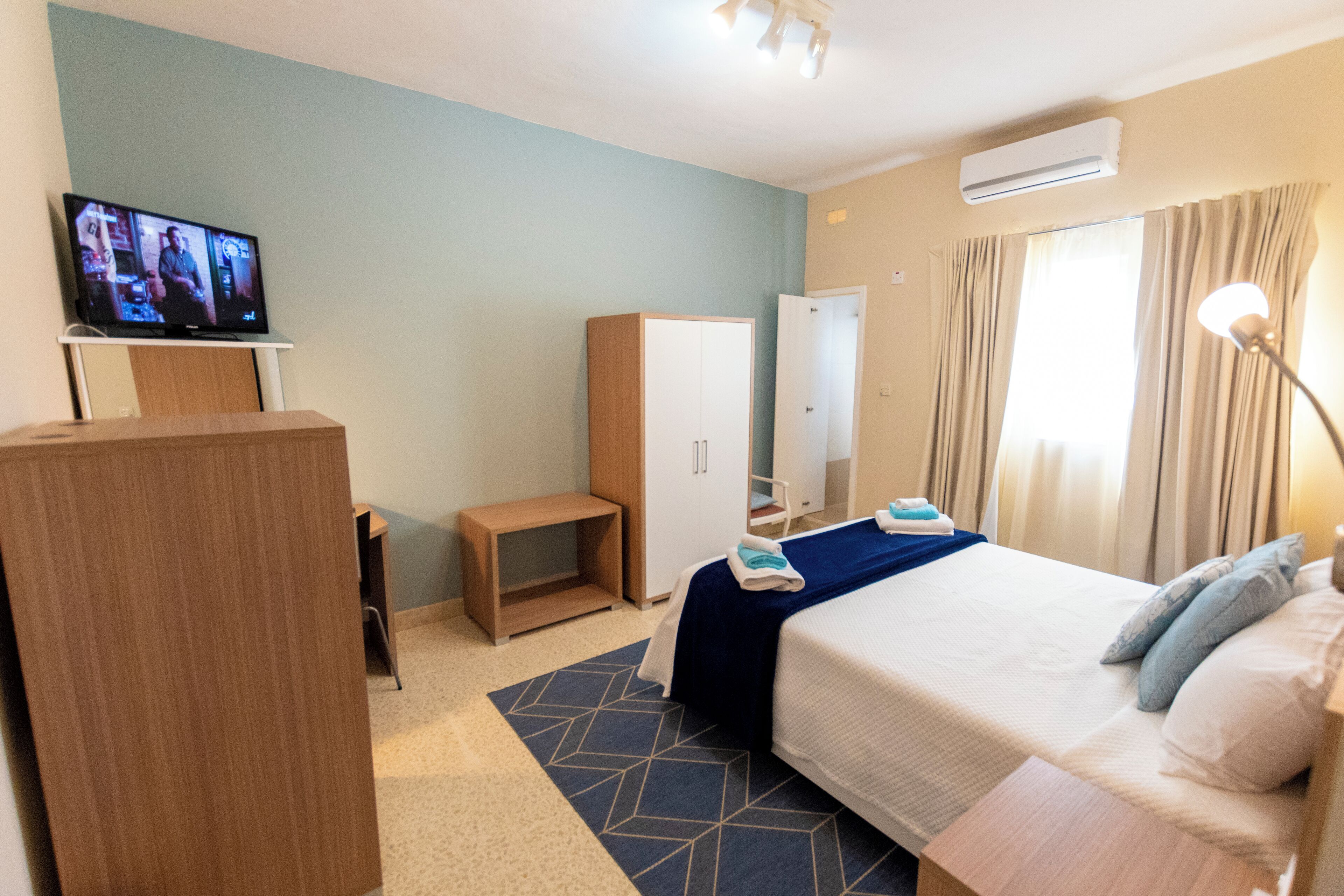 Habitación de hotel con cama, escritorio, armario, televisor y aire acondicionado.
