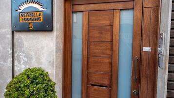 Uma entrada moderna com porta de madeira, uma placa de metal acima e um vaso de planta ao lado da porta.