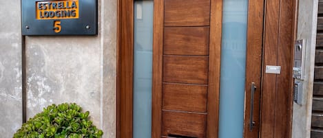 A modern entrance with a wooden door, a metal sign above it, and a potted plant beside the door.