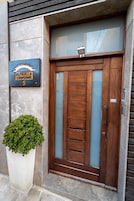 Una entrada moderna con puerta de madera, un cartel metálico encima y una planta en maceta al lado.